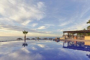 An infinity pool with a clear view of the ocean, palm trees, and a covered outdoor seating area. - Grand Fiesta Americana Los Cabos All Inclusive Golf & Spa (Cabo San Lucas)
