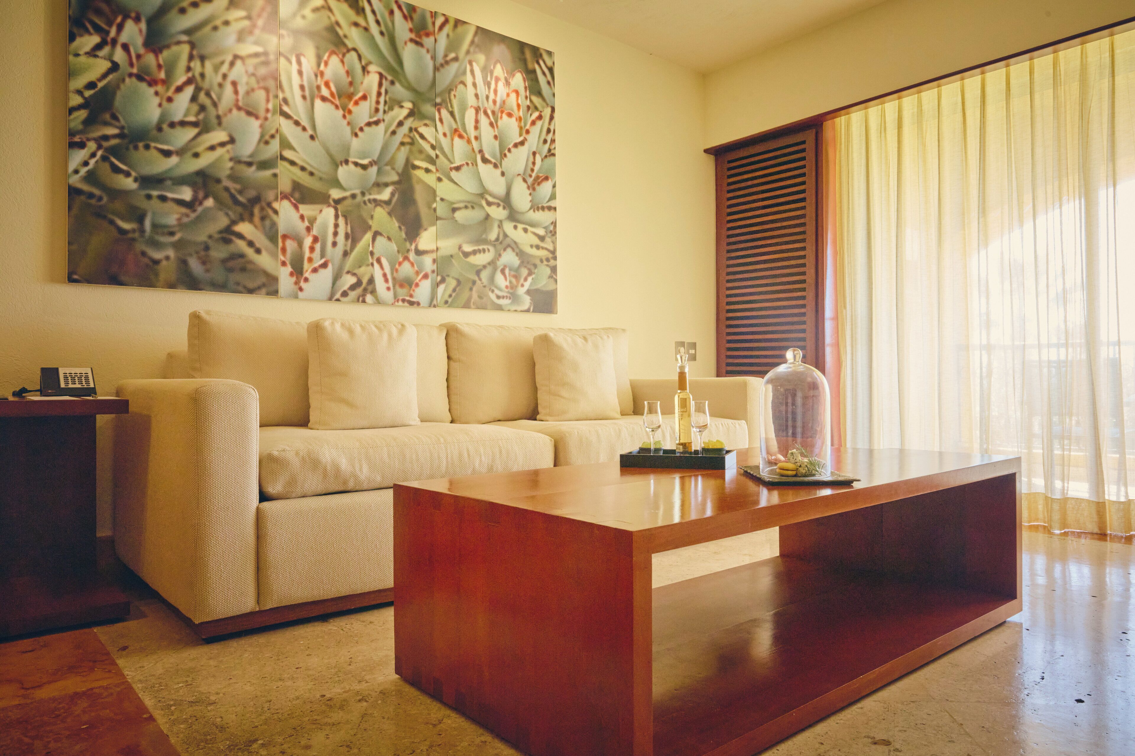 A living room with a sofa, a wooden coffee table, a painting on the wall, and a window with blinds.