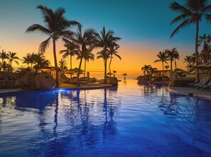 A resort pool with palm trees and lounge chairs, surrounded by large rocks and a sunset view. - Grand Fiesta Americana Los Cabos All Inclusive Golf & Spa (Cabo San Lucas)