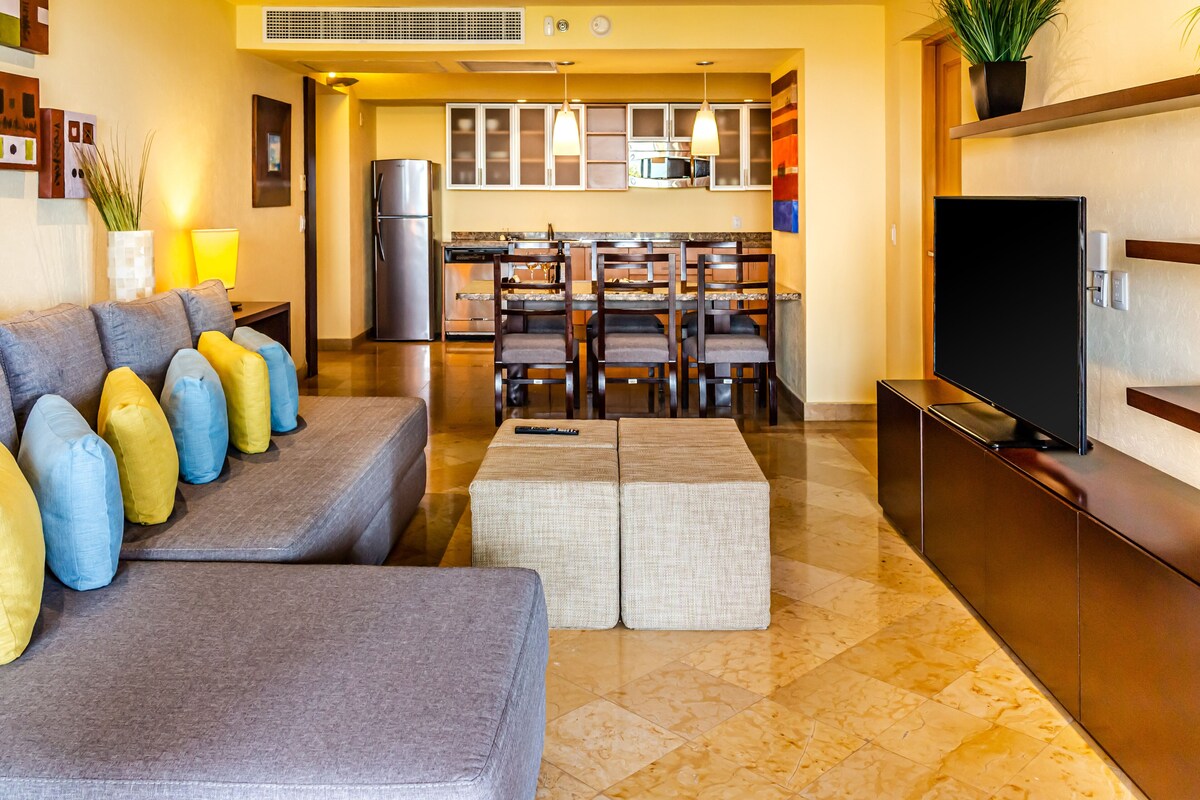 A modern living room with a sofa, ottoman, and a flat-screen TV.