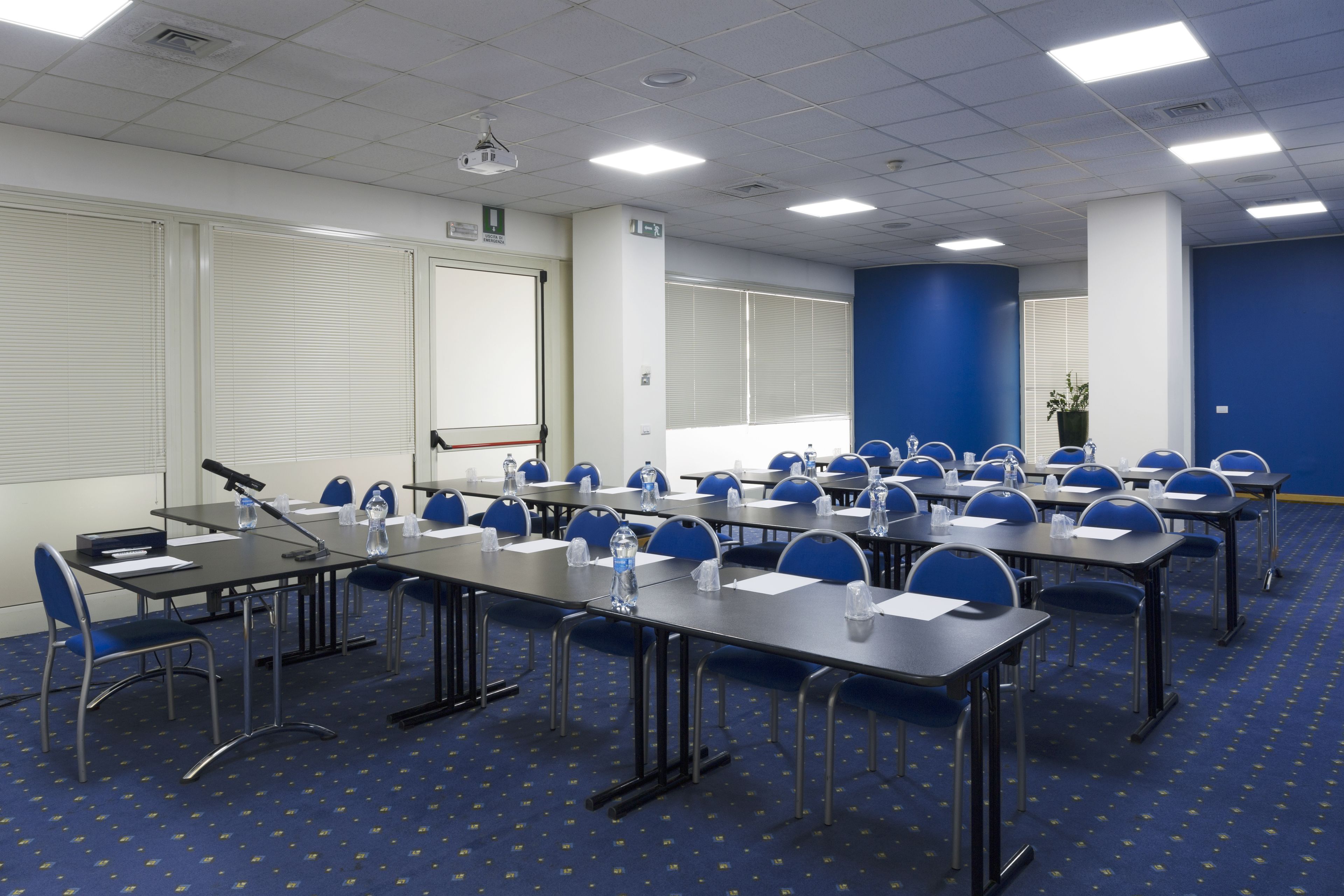 A conference room with rows of tables and chairs, a projector, and a large screen.