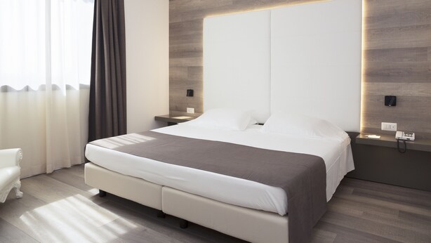 A modern bedroom with a large bed, bedside tables, and a neutral color scheme. - City Hotel & Suites Foligno (Foligno)