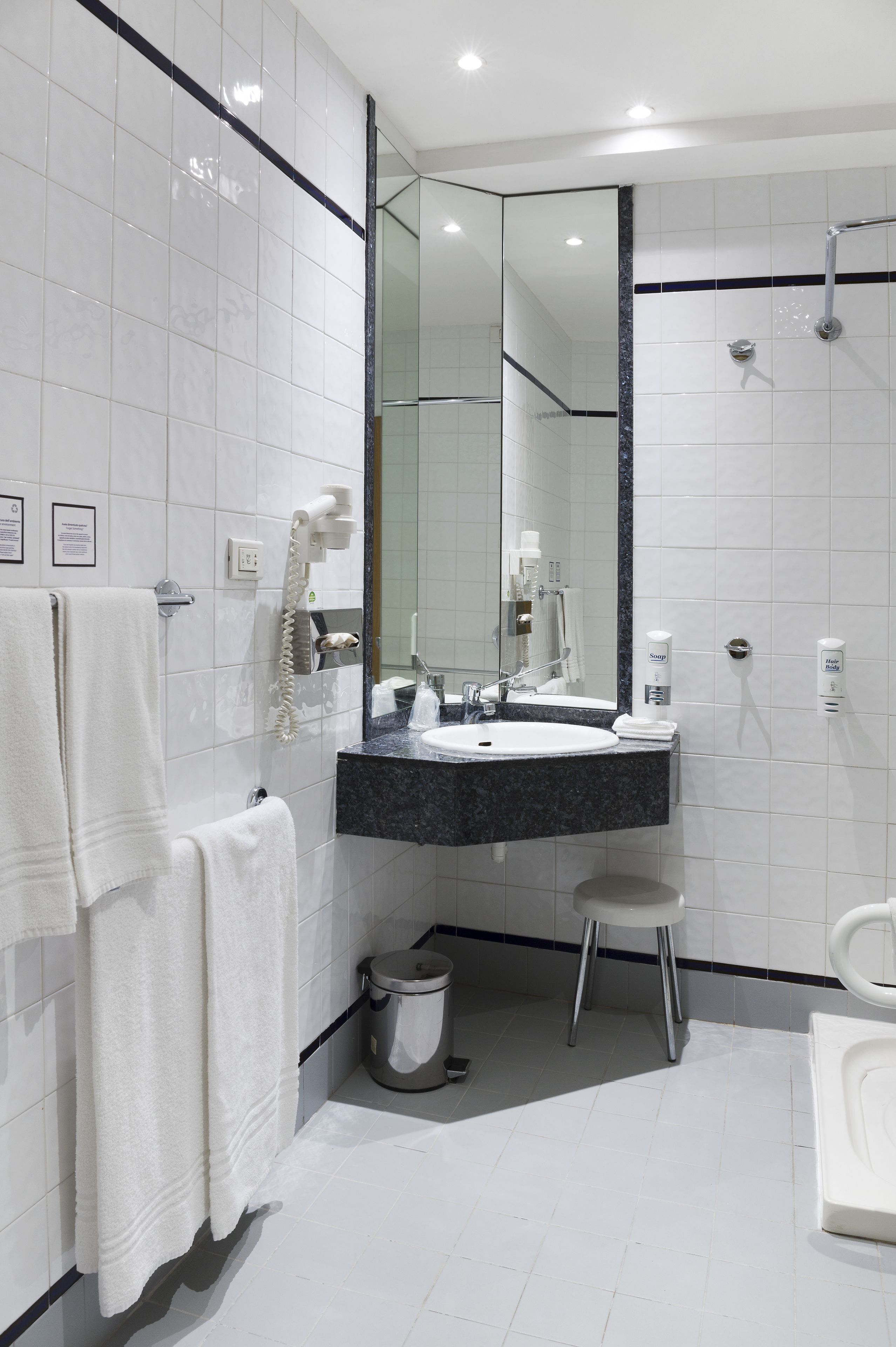 A modern bathroom with white tiles, a large mirror, a sink, a shower, and a toilet.