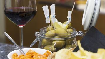 Un verre de vin rouge, un bocal d’olives, un bol de pâtes et un panier de chips sur une table.