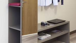 A wardrobe with a wooden door, a hanging rack, and shelves with a camera and magazines. - City Hotel & Suites Foligno (Foligno)