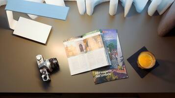 A table with a camera, brochures, a glass of orange juice, and a white envelope.