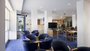 A hotel lobby with blue carpet, a reception desk, a television, and seating areas. - City Hotel & Suites Foligno (Foligno)