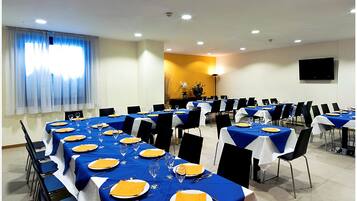 Een vergaderzaal met tafels gedekt voor een formeel evenement, met blauwe tafelkleden, witte stoelen en netjes opgemaakte zitplaatsen.