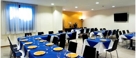A conference room with tables set for a formal event, featuring blue tablecloths, white chairs, and neatly arranged place settings.