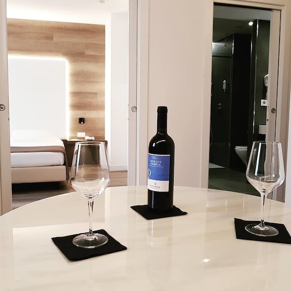 A hotel room with a round table, two wine glasses, and a bottle of Merlot Umbria wine. - City Hotel & Suites Foligno (Foligno)