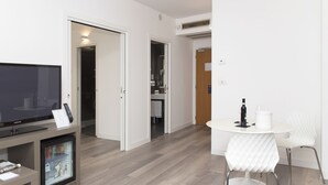 A modern living room with a flat-screen TV, a small refrigerator, a coffee machine, and a white dining table with chairs. - City Hotel & Suites Foligno (Foligno)
