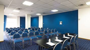 A conference room with rows of blue chairs, tables with water bottles, and a blue carpeted floor.