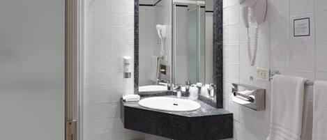 A modern bathroom with a double sink, a hairdryer mounted on the wall, and a towel rack.