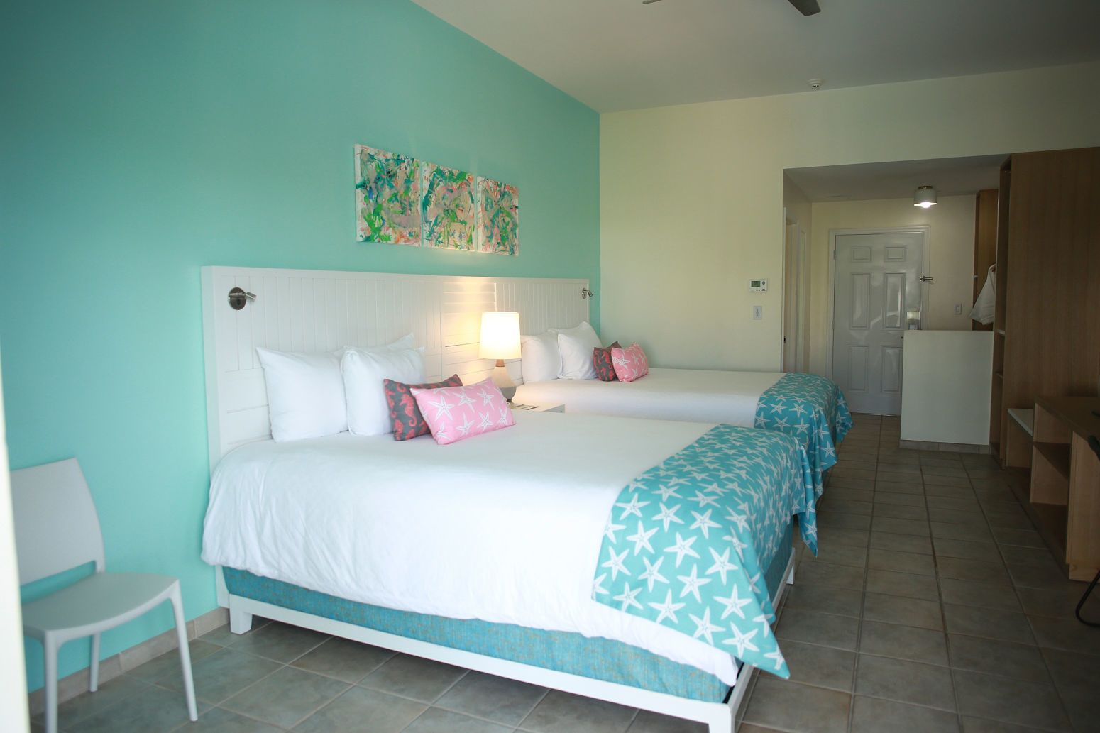 A bedroom with two beds, a nightstand, a chair, and a door leading to a bathroom.