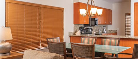A modern kitchen with wooden cabinets, a granite countertop, and a dining area with wicker chairs and a glass table.