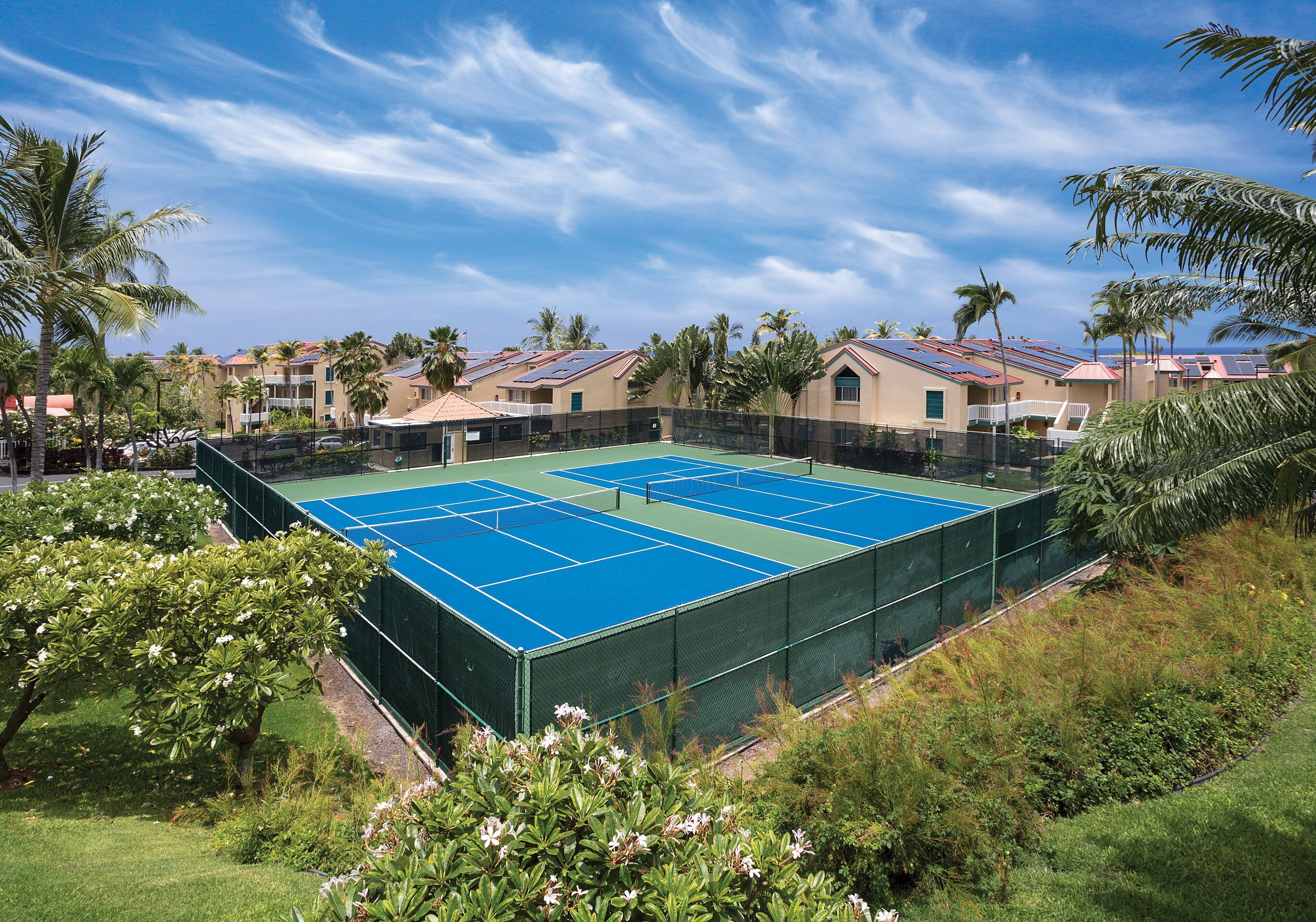 A tennis court surrounded by greenery and buildings with red roofs.
