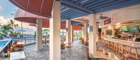 An outdoor patio area with tables and chairs, a pool, and a bar.