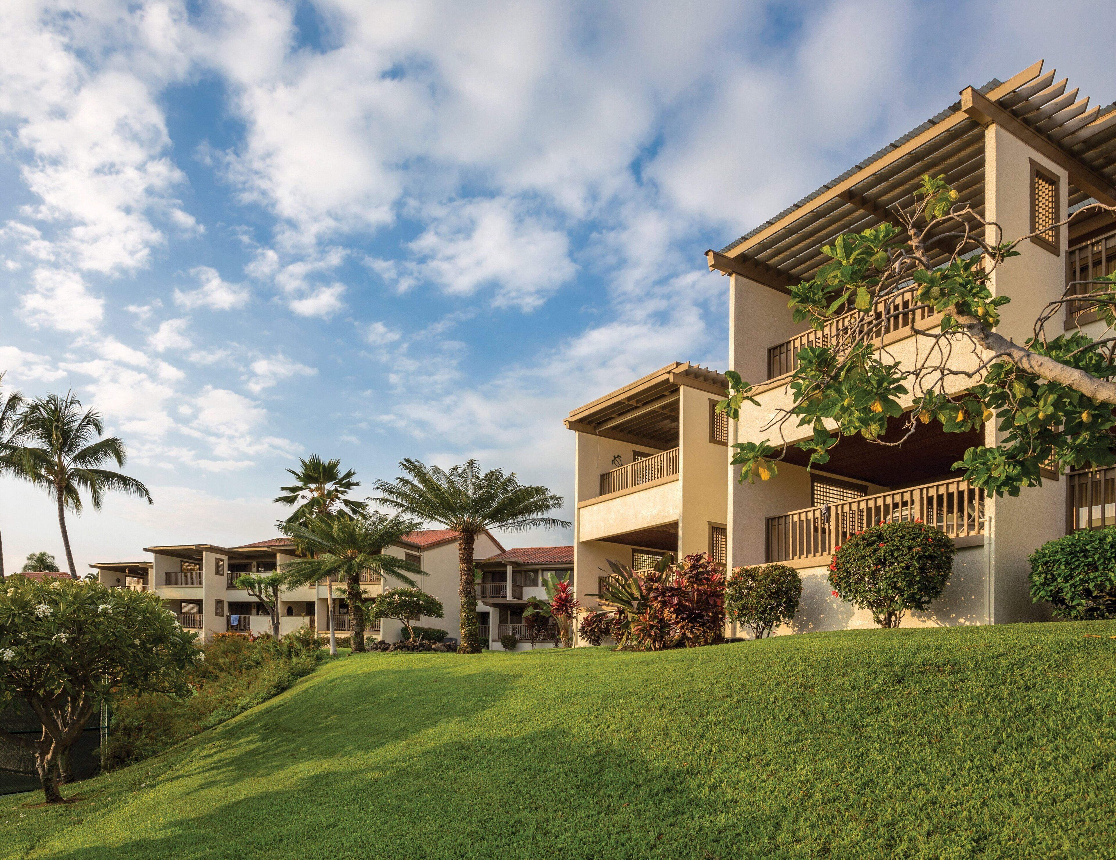 A multi-story hotel with balconies, lush greenery, and a clear sky.