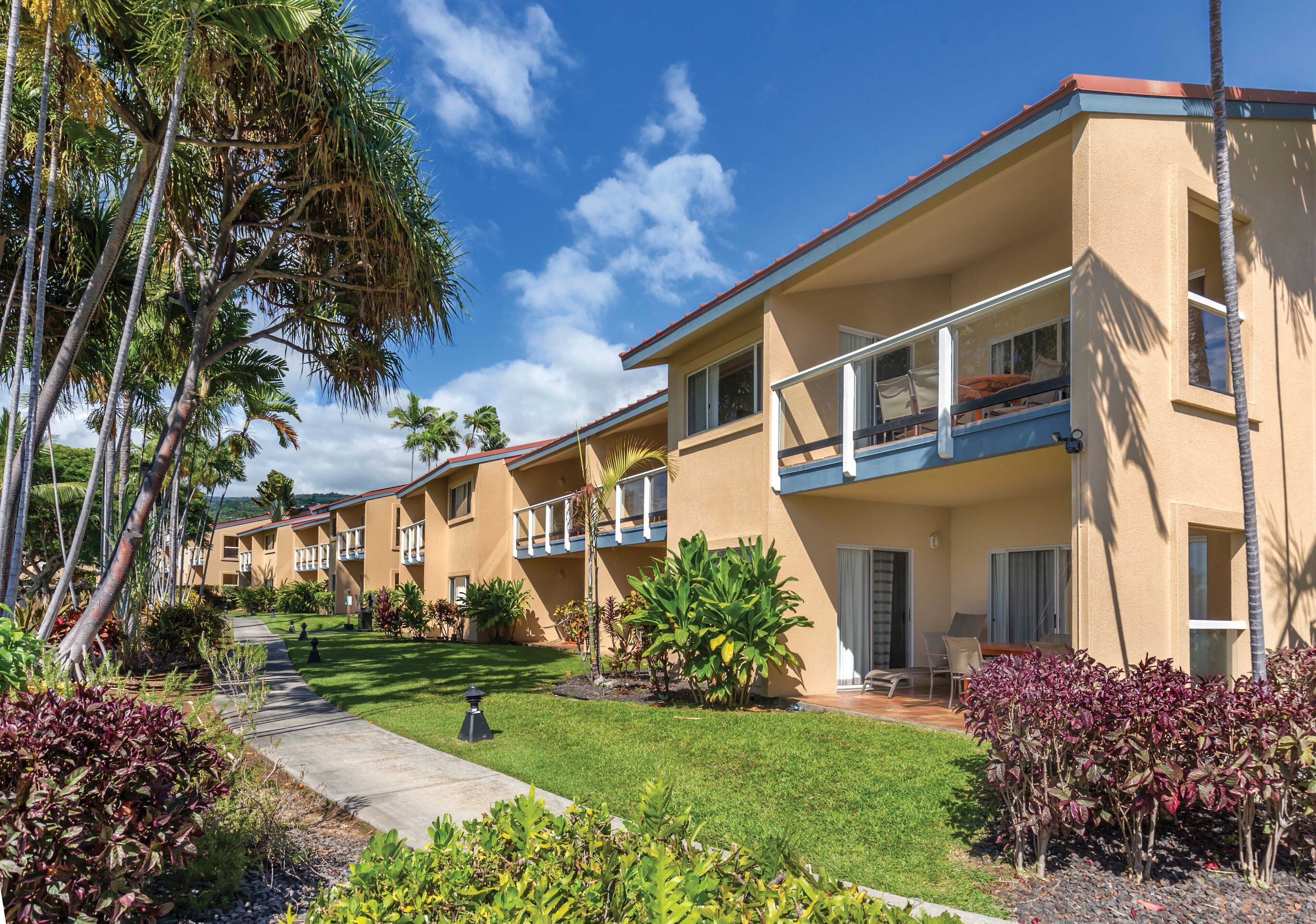 A hotel with multiple balconies, a well-maintained lawn, and tropical landscaping.