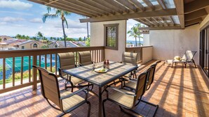 A covered outdoor patio with a table and chairs, overlooking a pool and a view of houses.