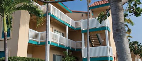 Un hotel de varios pisos con balcones, palmeras y un cielo despejado.