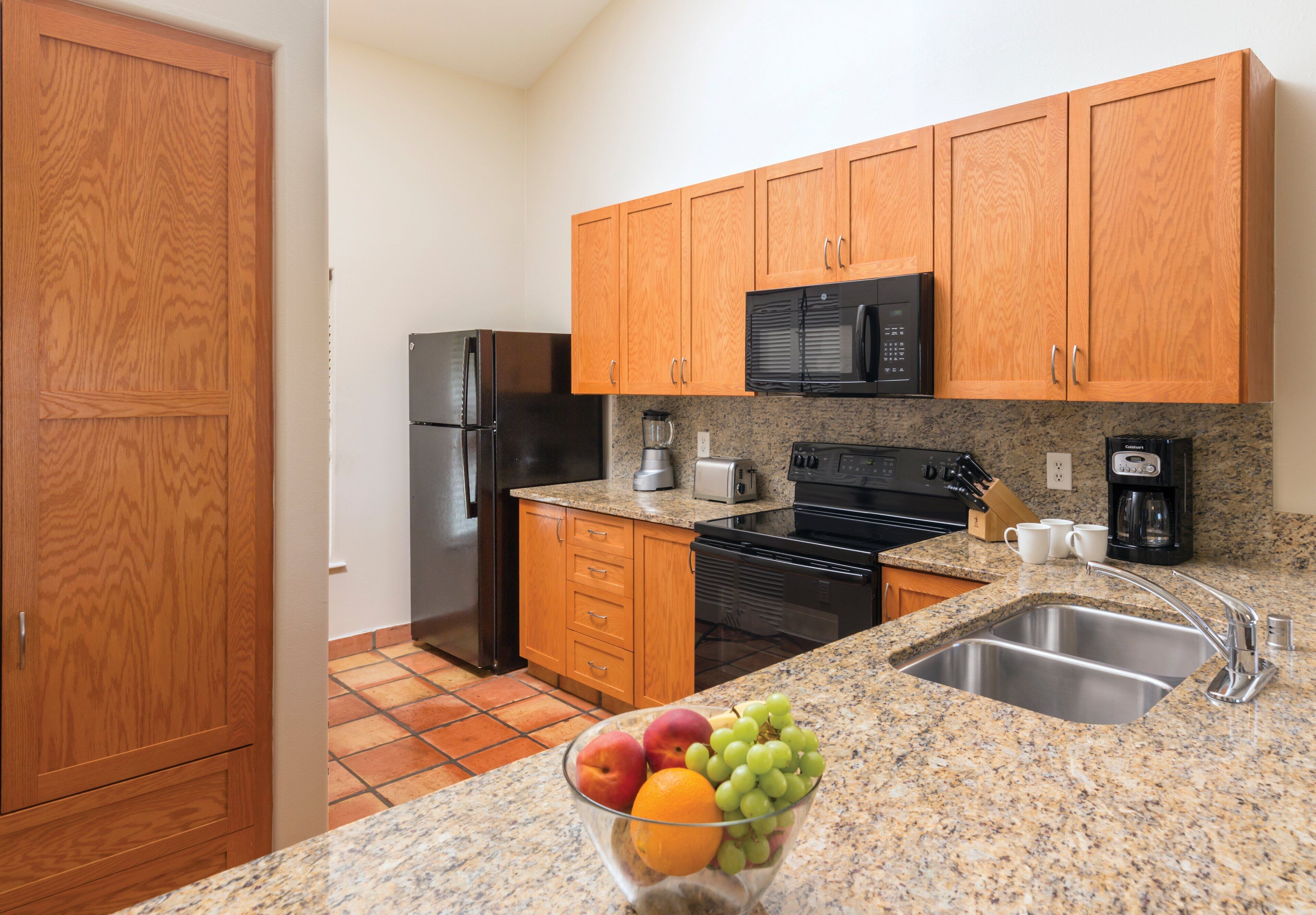 A kitchen with wooden cabinets, a stainless steel sink, a granite countertop, a black refrigerator, a black oven, and a coffee maker.