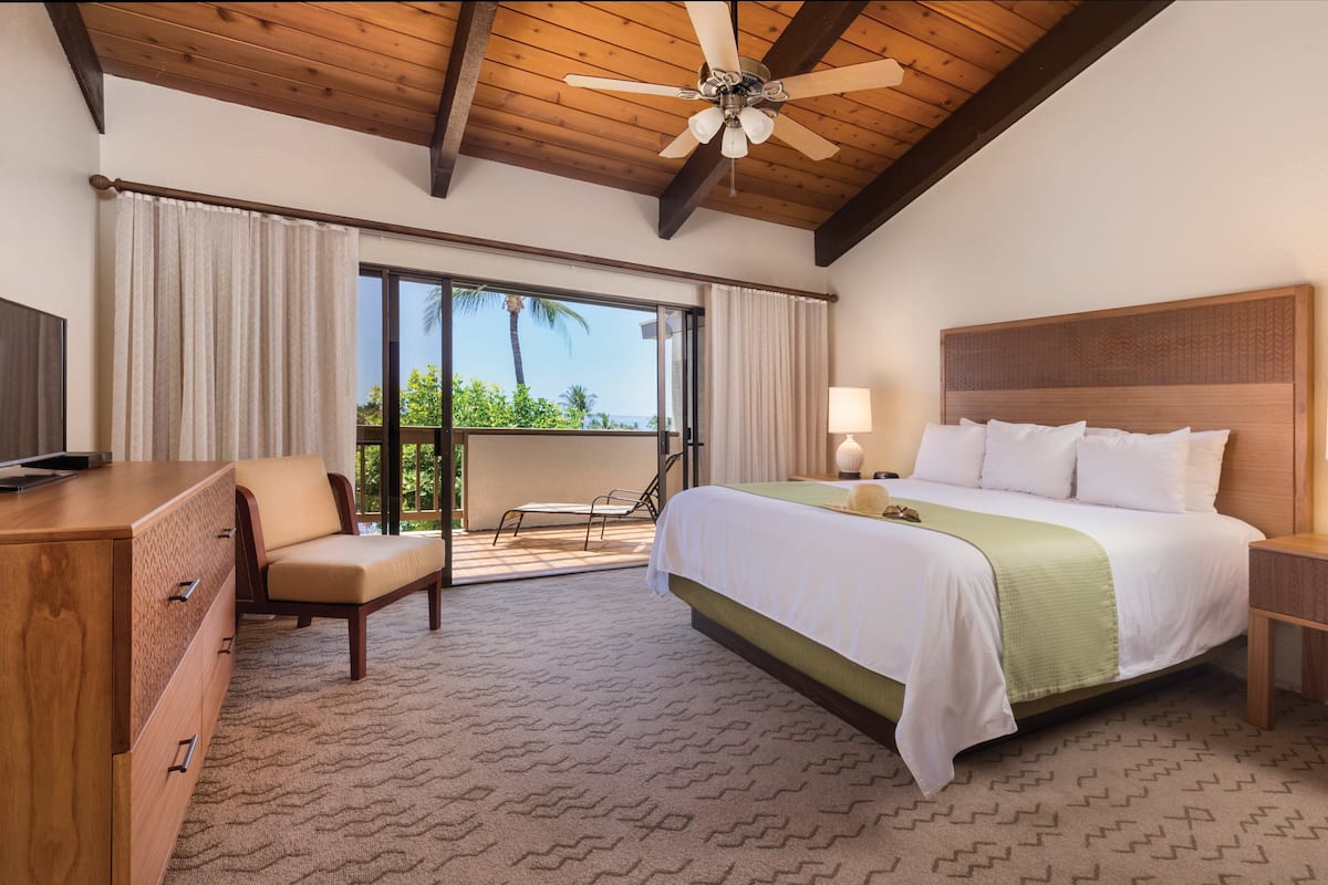Ein Hotelzimmer mit Bett, Schreibtisch, Stuhl, Deckenventilator und Blick ins Freie.
