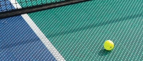 Primer plano de una cancha de tenis con una pelota amarilla cerca de la red.