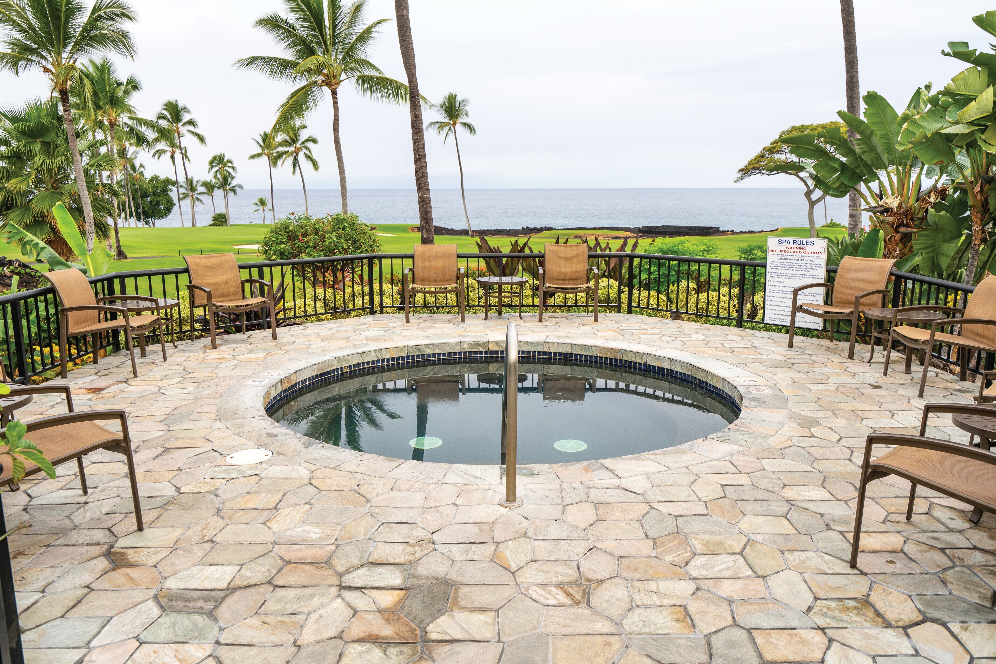 A pool area with stone flooring, surrounded by chairs and a signboard.