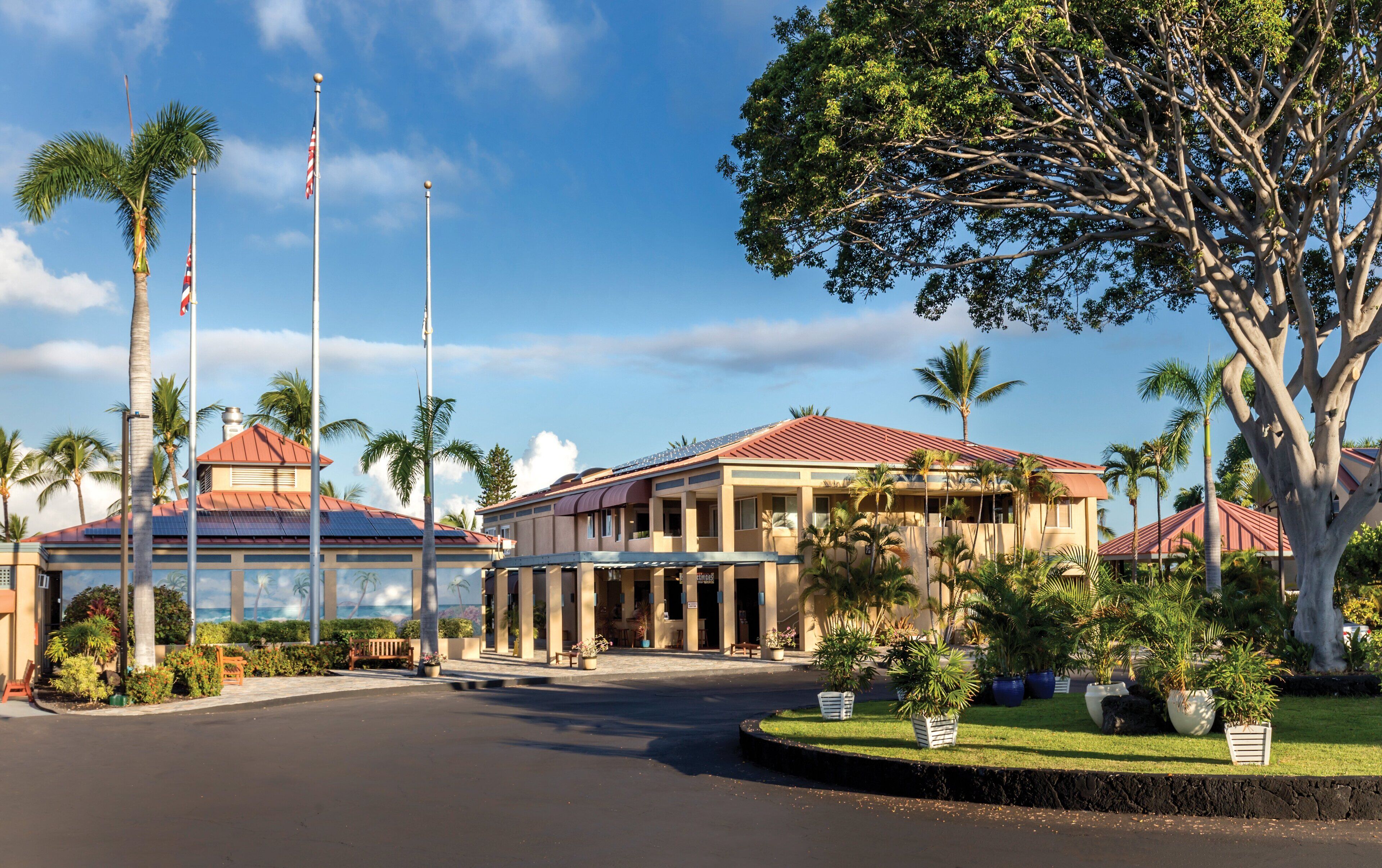 A hotel with a red-roofed building, palm trees, and a clear sky.