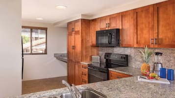 A kitchen with wooden cabinets, granite countertops, stainless steel appliances, and a window with blinds.