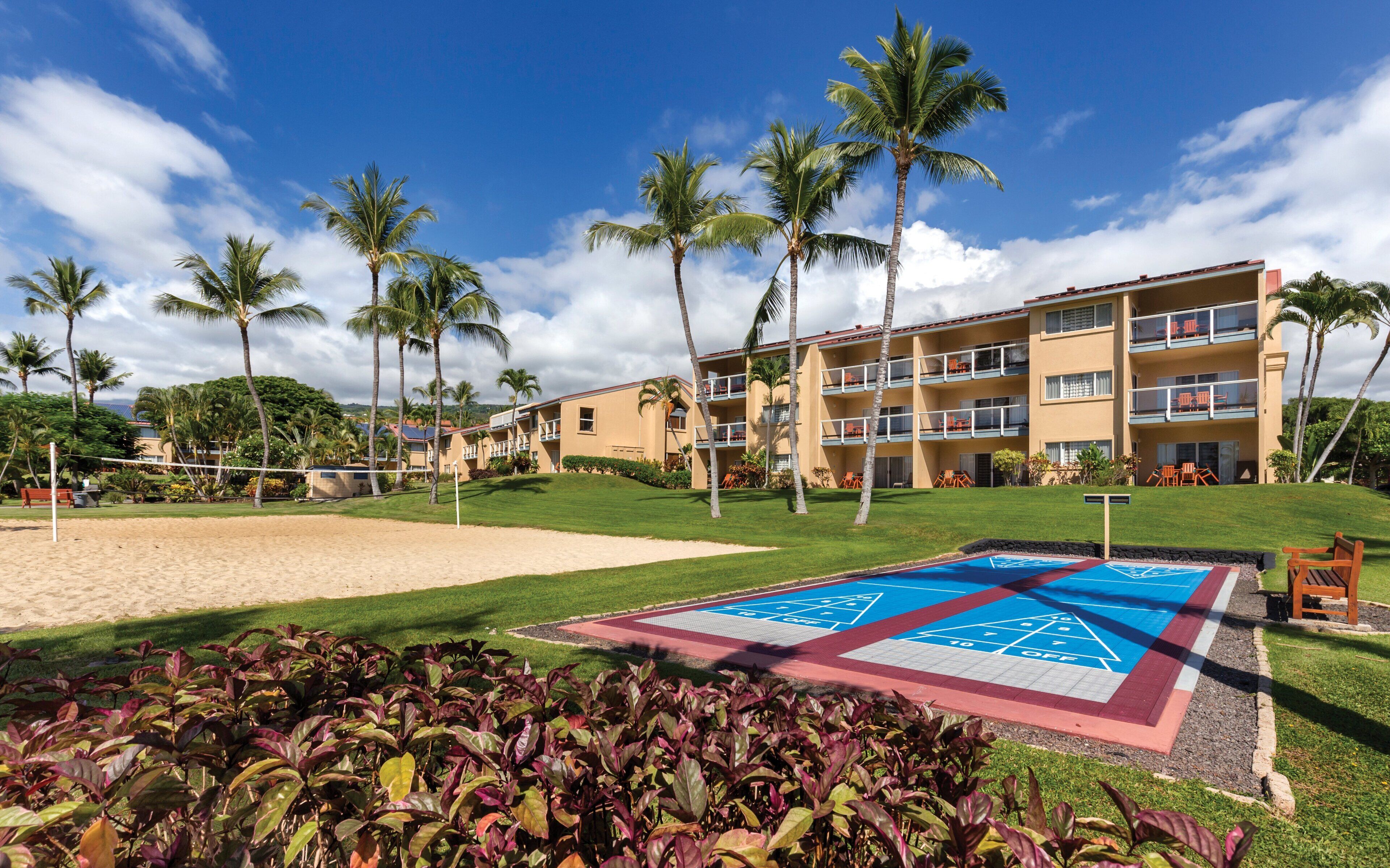 Ein Hotel mit mehreren Balkonen, einem Poolbereich mit Shuffleboard und Palmen.