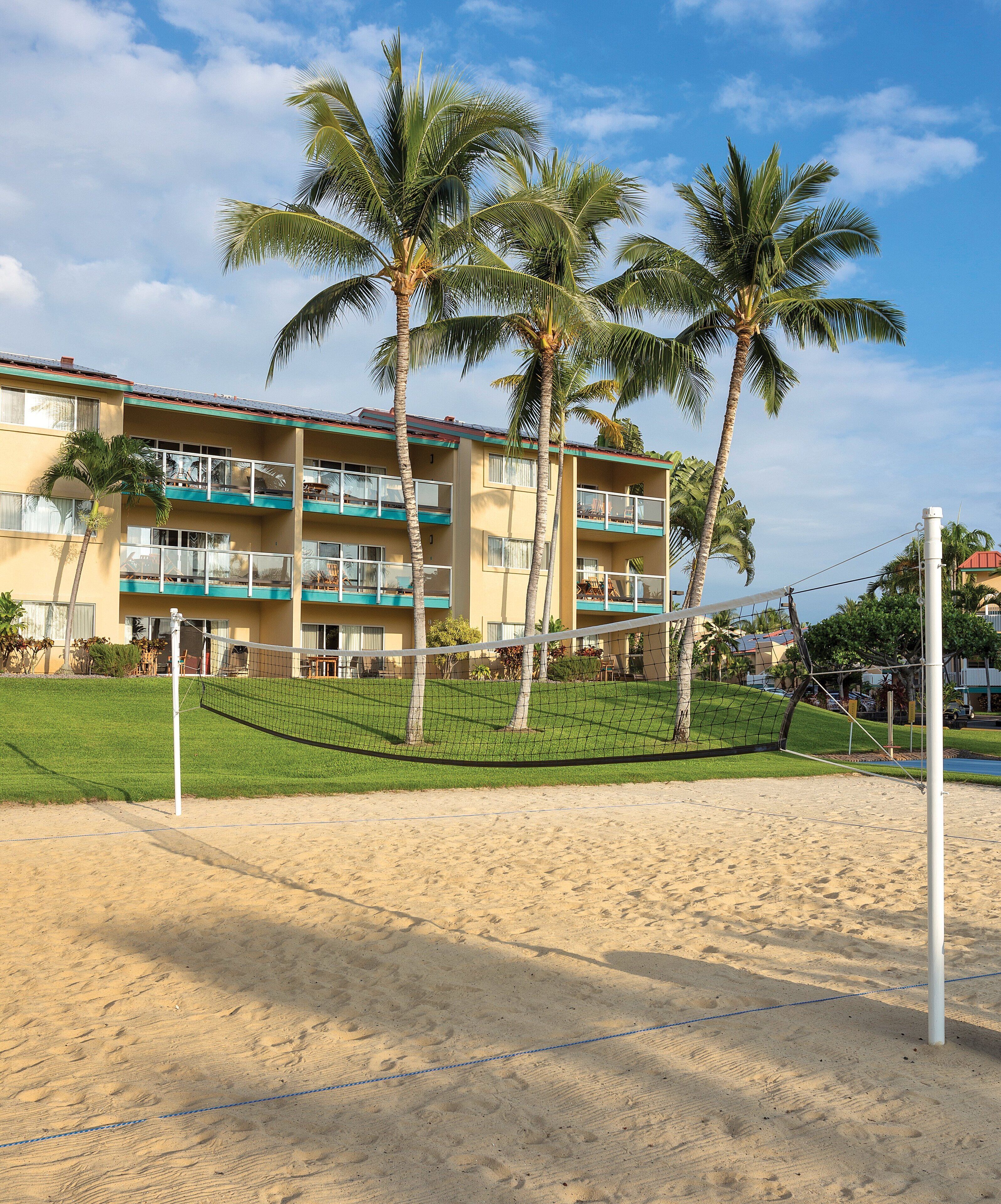 Ein Beachvolleyballfeld mit Netz, Palmen und einem Hotel im Hintergrund.