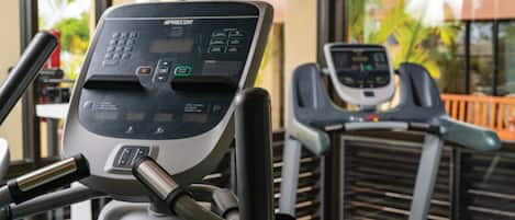 Ett gym med löpband och annan träningsutrustning, stora fönster och utsikt över palmer.