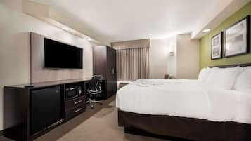 Une chambre d’hôtel comprenant un lit, un bureau avec un téléviseur à écran plat, une chaise, une armoire et une fenêtre avec des rideaux.