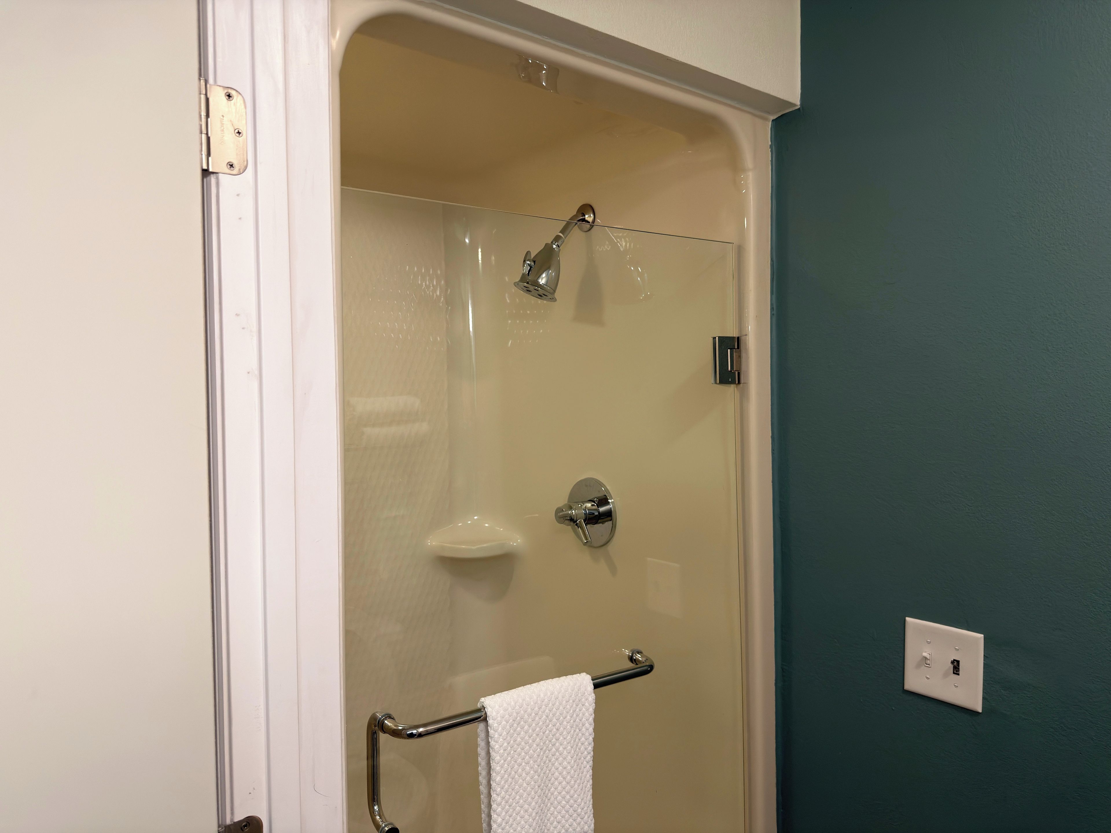 A glass-enclosed shower with a handheld showerhead and a handheld faucet.