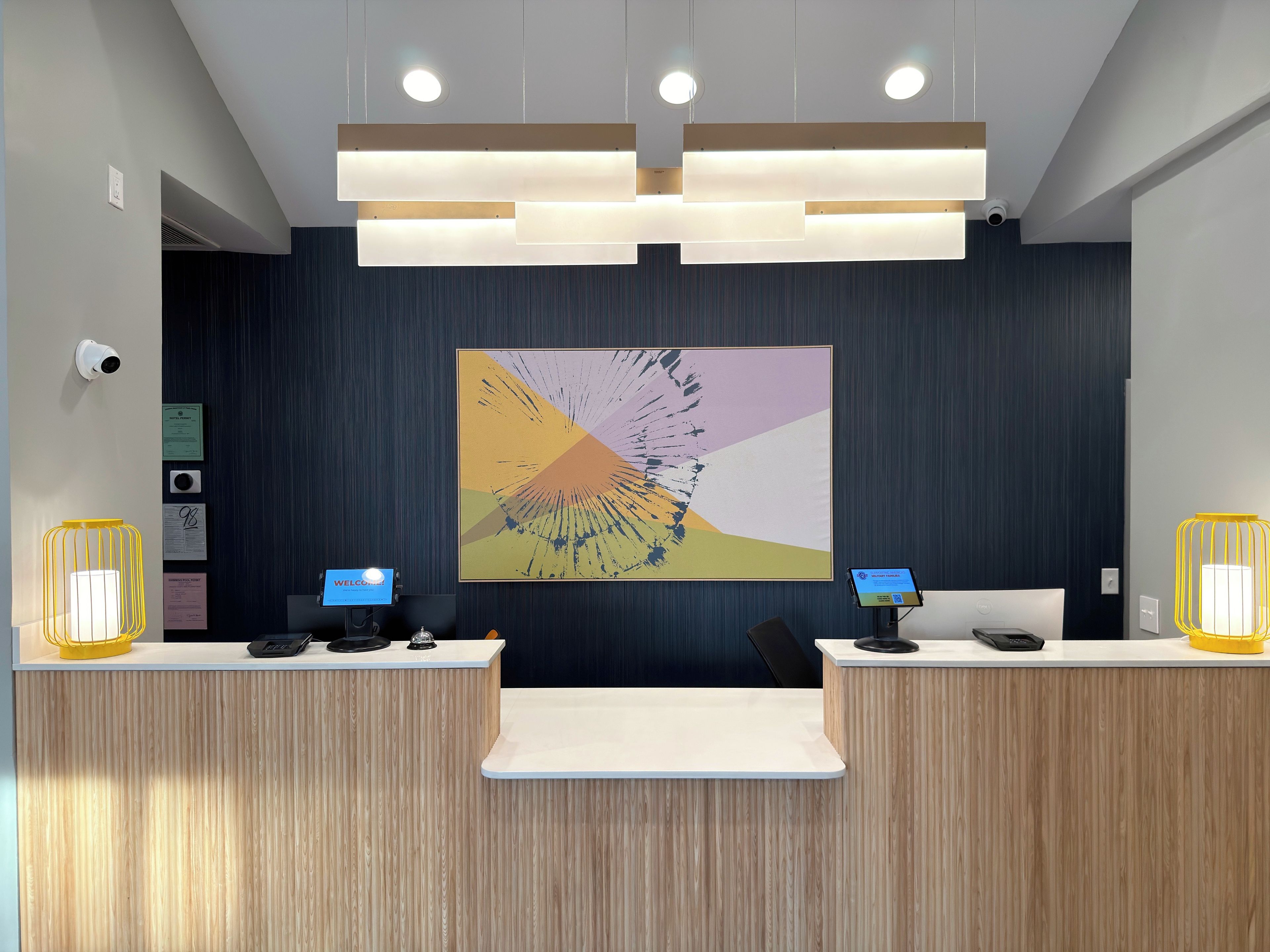 Bancada de recepção com dois monitores de computador, uma grande pintura abstrata e uma câmera de segurança.