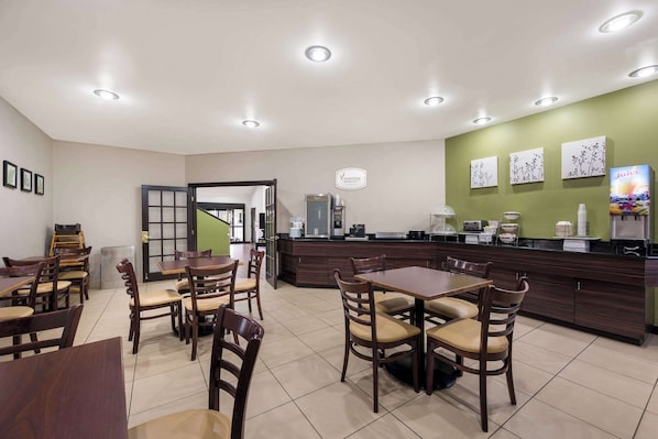 A modern cafe with wooden tables and chairs, a counter with a coffee machine, and artwork on the walls.