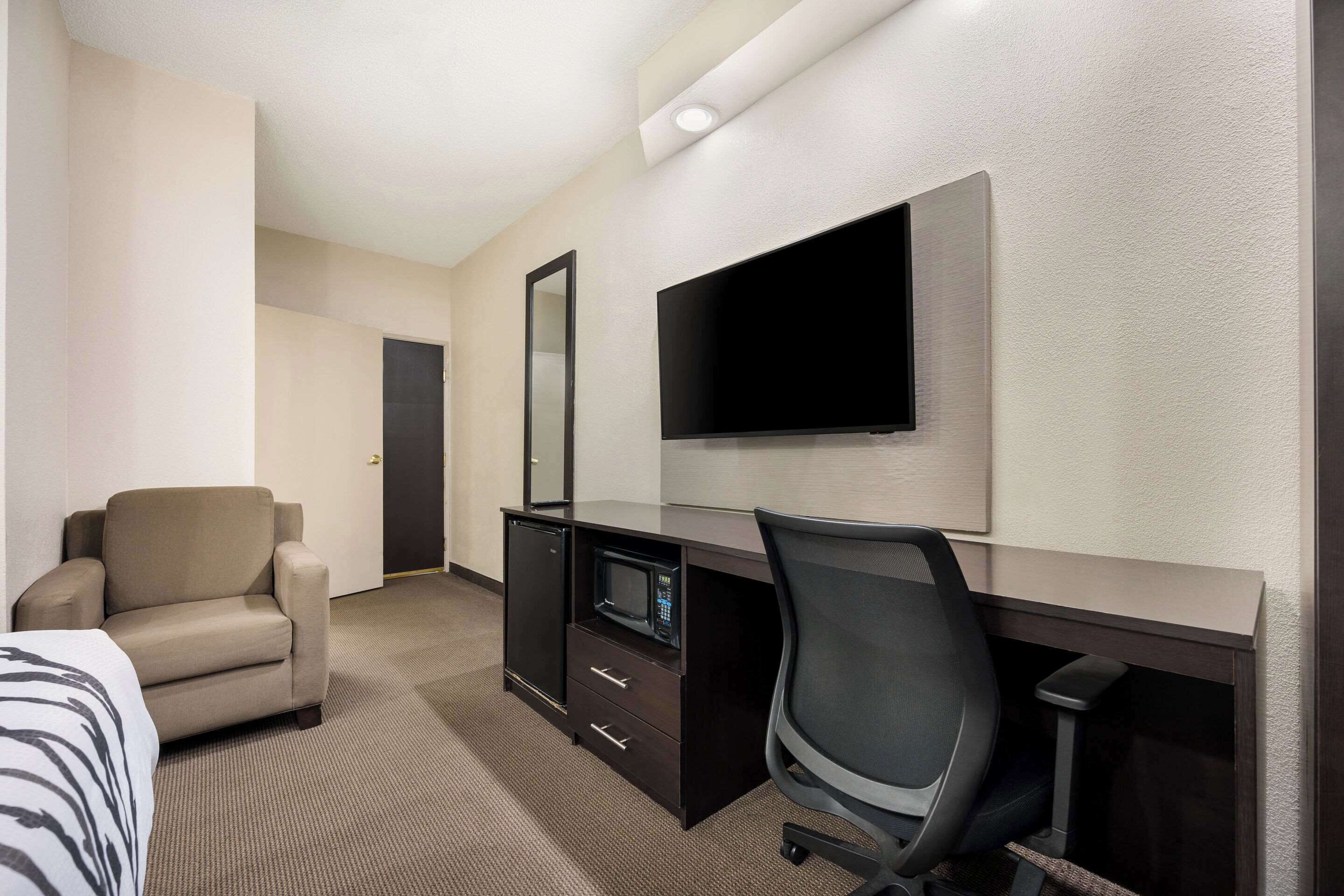 Habitación de hotel con cama, escritorio con computadora y televisor de pantalla plana, una silla y un microondas.