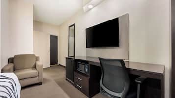 A hotel room with a bed, a desk with a computer and a flat-screen TV, a chair, and a microwave.