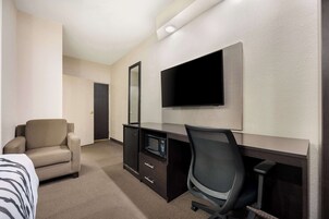 Habitación de hotel con cama, escritorio con computadora y televisor de pantalla plana, una silla y un microondas.