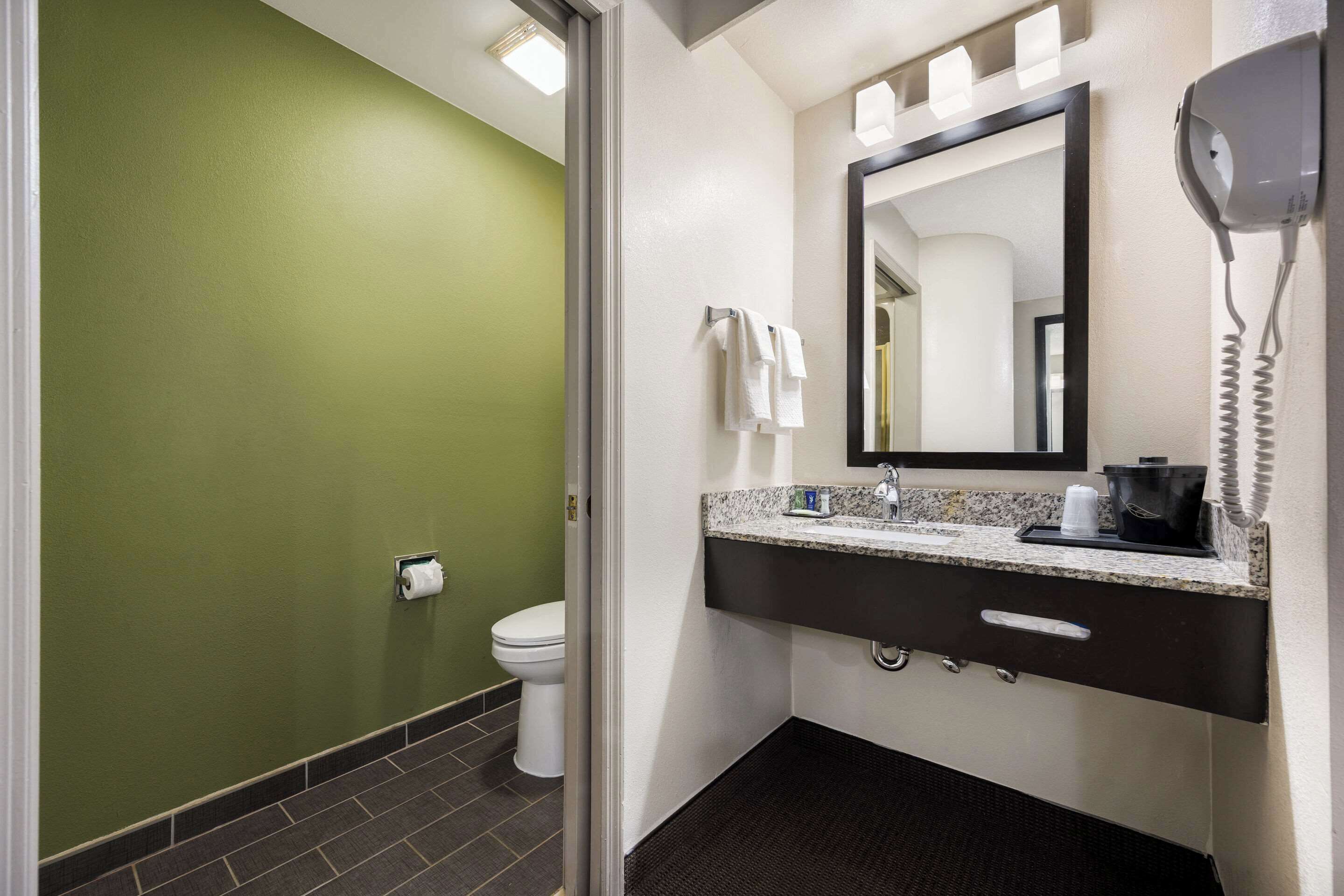A bathroom with a green wall, a white toilet, a sink with a mirror, and a hairdryer on the wall.