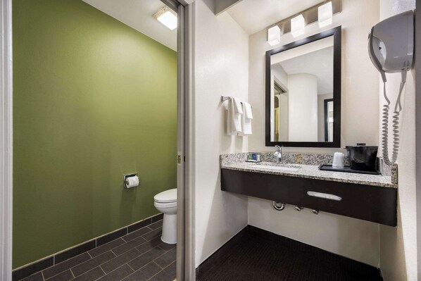 Une salle de bain avec un mur vert, des toilettes blanches, un lavabo avec un miroir et un sèche-cheveux fixé au mur.