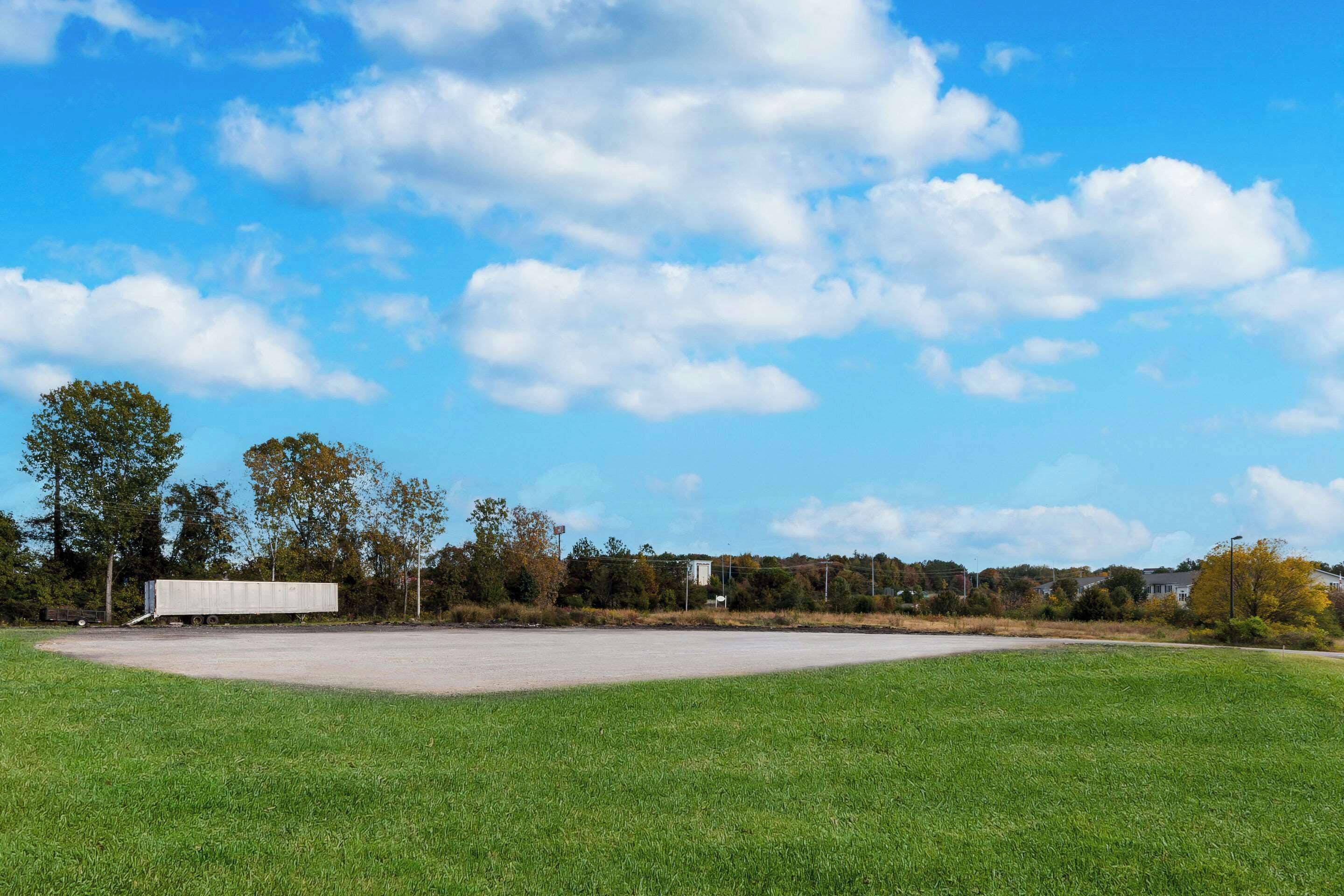 A large, open grassy field with a white trailer in the distance.
