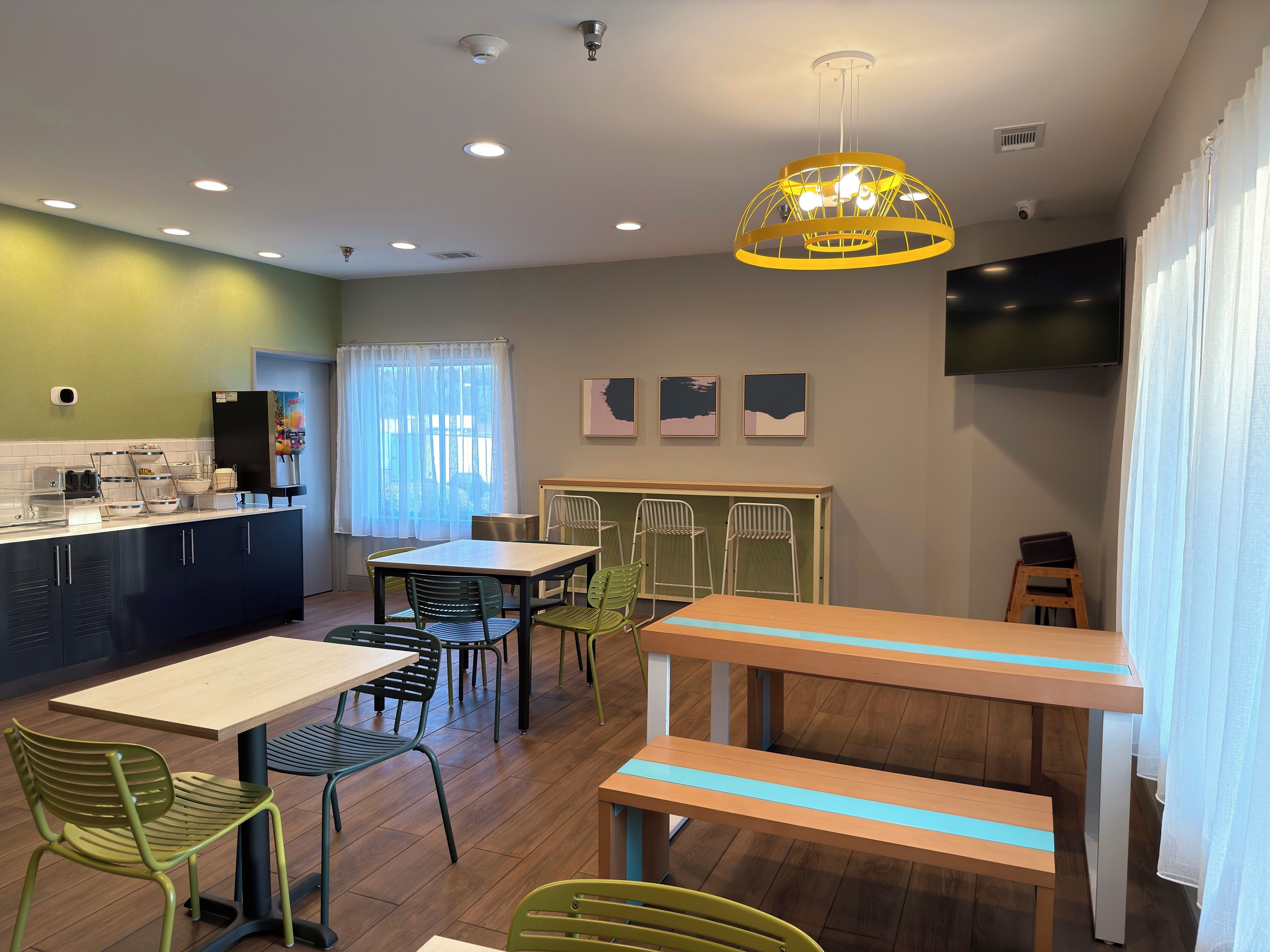 Un café moderno con una mesa y sillas de madera, una barra con una máquina de café y un televisor grande en la pared.
