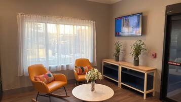 Een kamer met twee schommelstoelen, een ronde tafel met een vaas, een televisie aan de muur en een brandalarm.