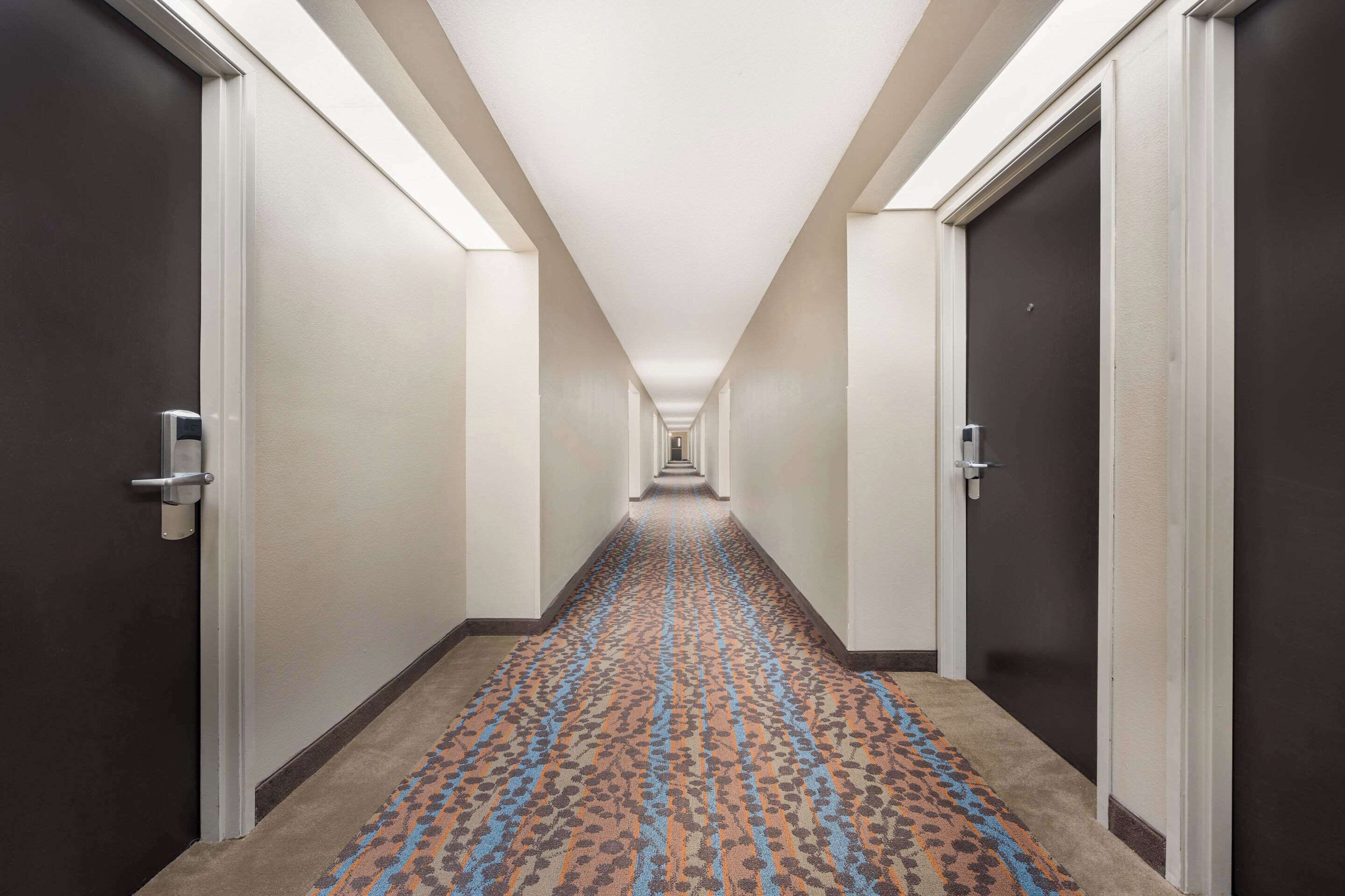 Un pasillo de hotel con pisos alfombrados, puertas a ambos lados y un camino iluminado que conduce a una escalera.