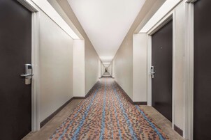 Un pasillo de hotel con pisos alfombrados, puertas a ambos lados y un camino iluminado que conduce a una escalera.