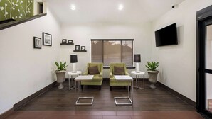A modern waiting area with two green armchairs, a flat-screen TV, and potted plants. - Sleep Inn Athens I-65 (Athens)
