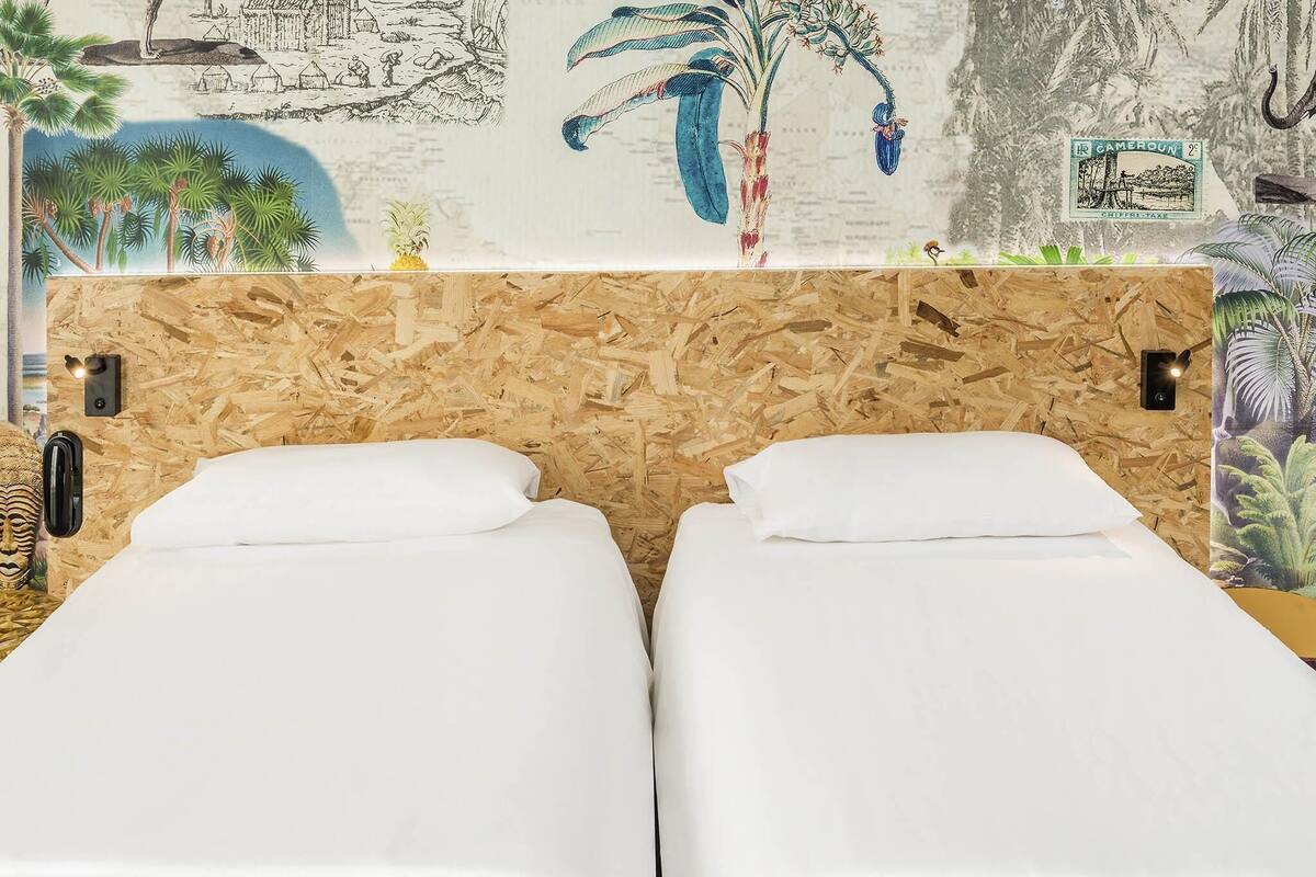 Een kamer met twee eenpersoonsbedden, een houten hoofdbord en een muurschildering met tropische en Afrikaanse elementen.